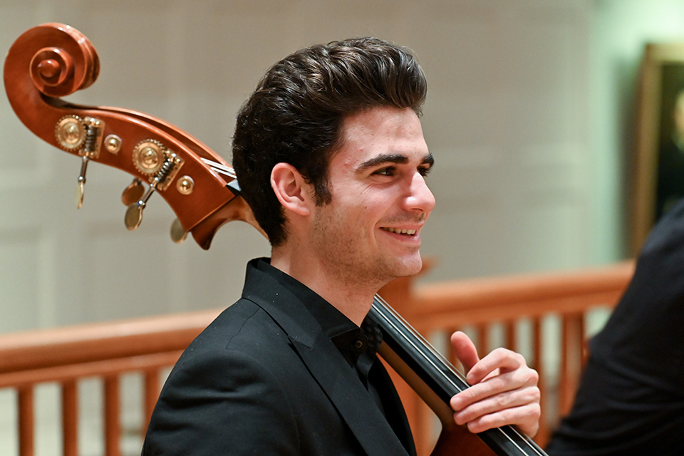 A male RCM student with dark hair smiles as he plays double bass
